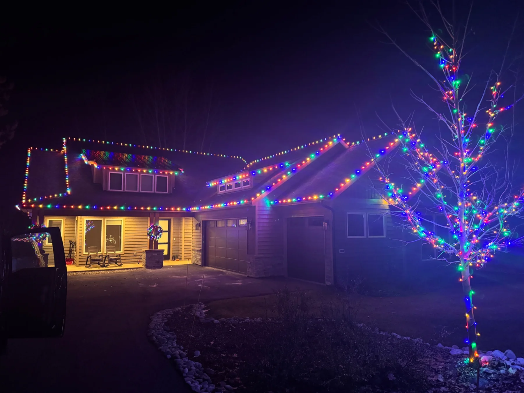 Multicolor Christmas lights across a home and front-yard tree